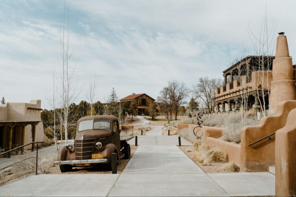 Unique wedding venue setting of a rustic outdoor scene at one of the Santa Fe wedding venues, featuring an old vintage truck parked on a pathway leading to adobe-style buildings.