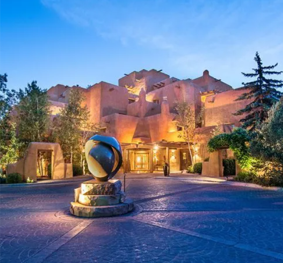 Stunning evening view of the Inn & Spa at Loretto, one of the premier Santa Fe wedding venues. The warm adobe architecture is beautifully lit against the twilight sky, with a distinctive sculpture in the foreground.