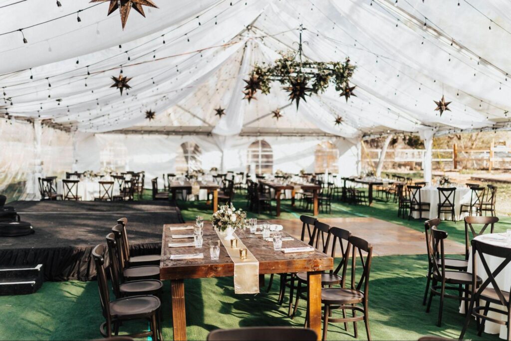 This photo captures a beautifully decorated wedding tent with elegant table settings, string lights, and star-shaped hanging ornaments, highlighting the meticulous planning that can make a significant difference when considering a wedding planner vs DIY wedding setup.