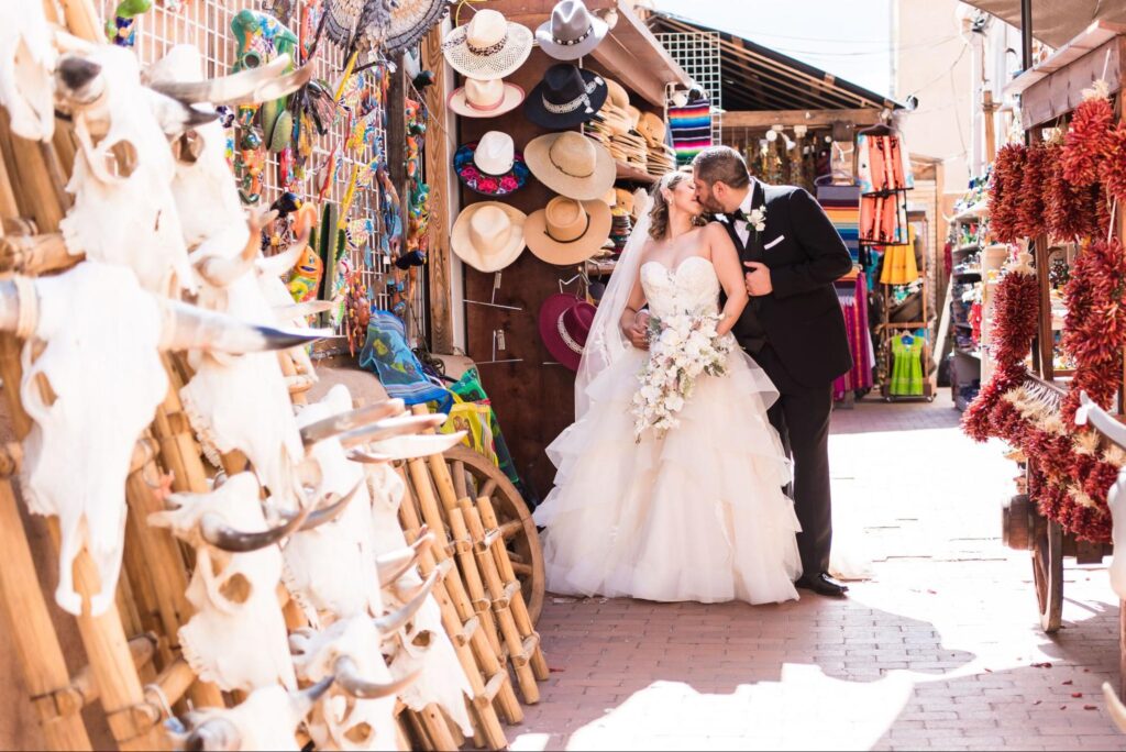 a couple in wedding attire embracing in a colorful marketplace, surrounded by Southwestern decor.