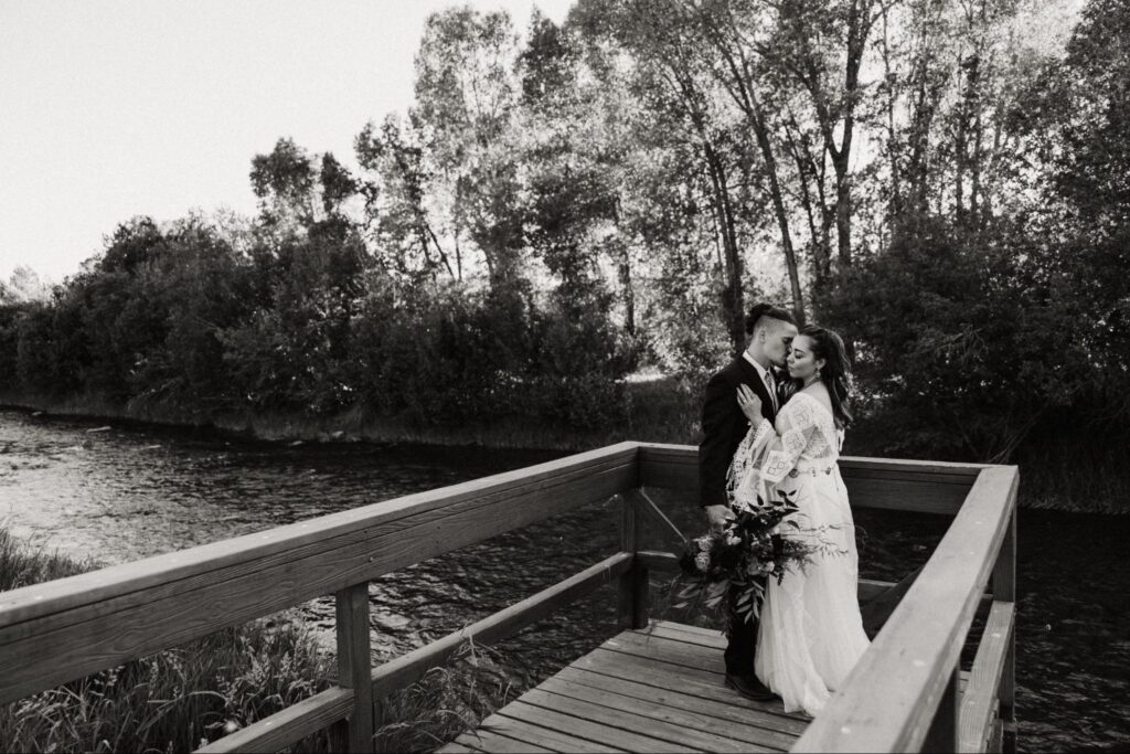 A romantic black-and-white moment of a couple on a riverside boardwalk