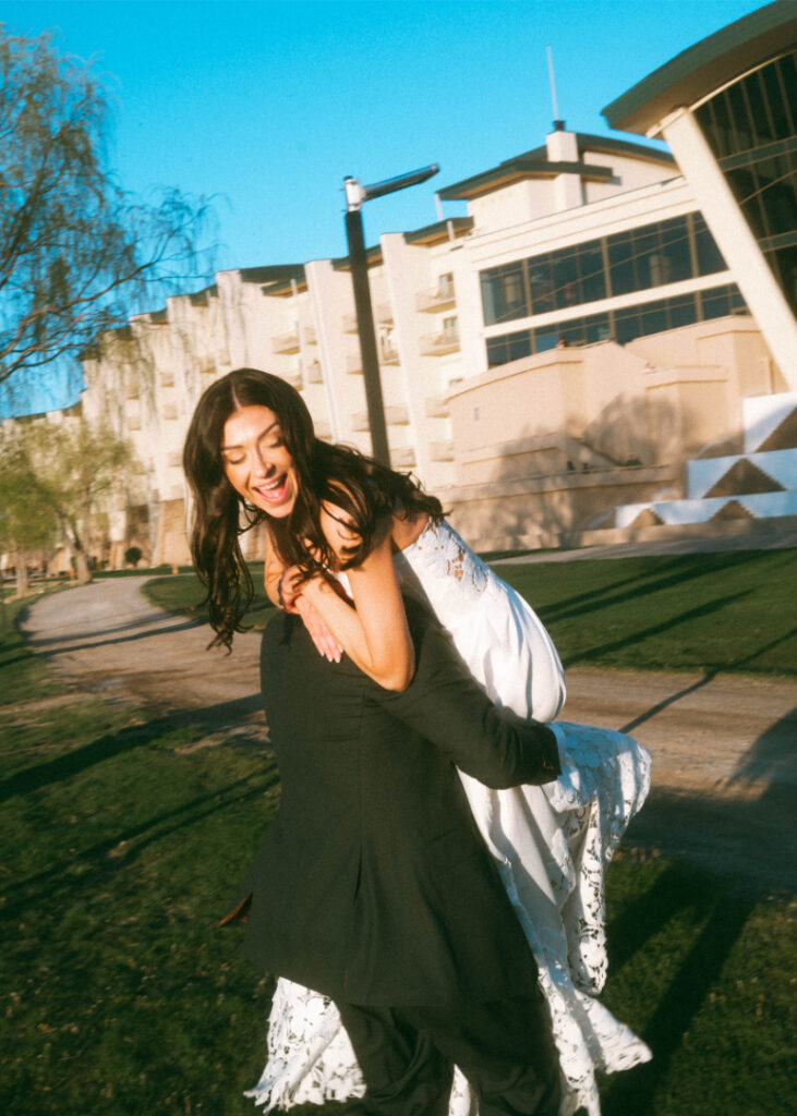 Groom carries bride over his should as they walk into reception venue after taking golden hour pictures at Inns of the Mountain Gods.