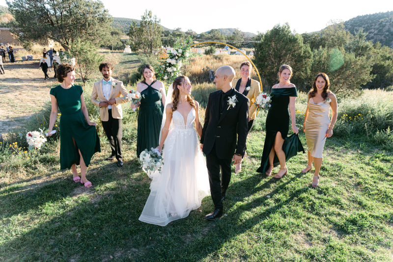 Bride and groom look at each other, walking hand in hand, as their wedding party walks behind them.