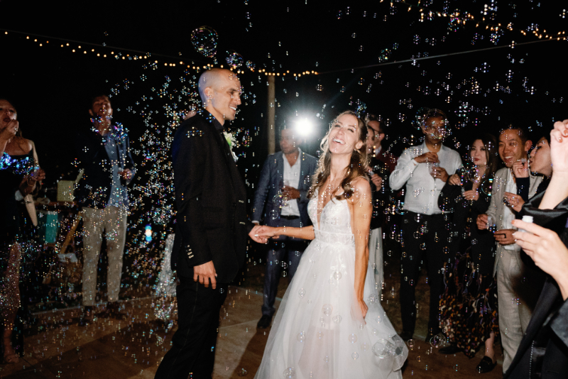 Bride and groom smiling as their reception guests blow bubbles as they make their grand exit during their non-traditional nuptials.