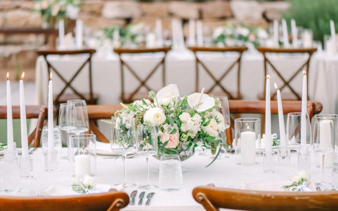 This photo features an elegant wedding table setting with a floral centerpiece, taper candles, glassware, and wooden chairs, showcasing a beautiful and romantic ambiance. Set up by a New Mexico wedding planner.