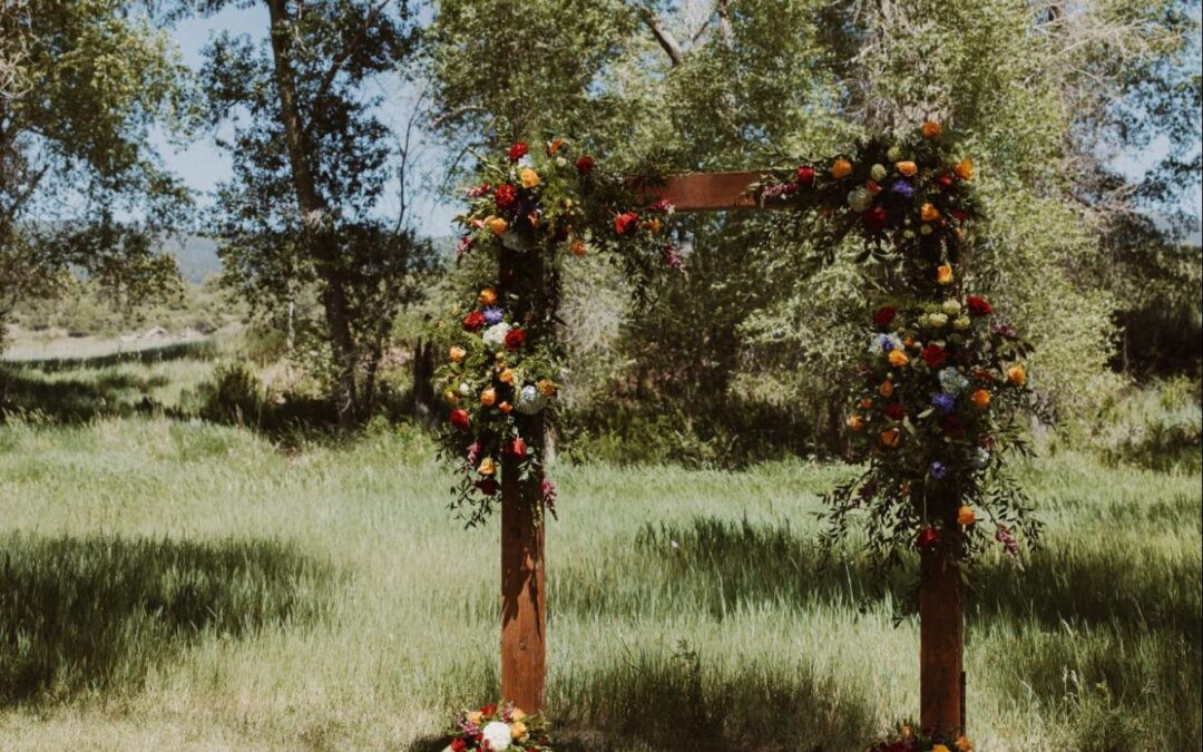 a rustic outdoor wedding arch adorned with vibrant floral arrangements, set in a natural grassy landscape | wedding planning guide