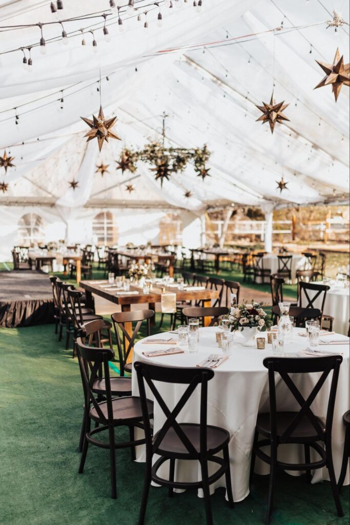 Wedding reception inside a clear tent decorated with hanging star lanterns, string lights, and elegant round tables.