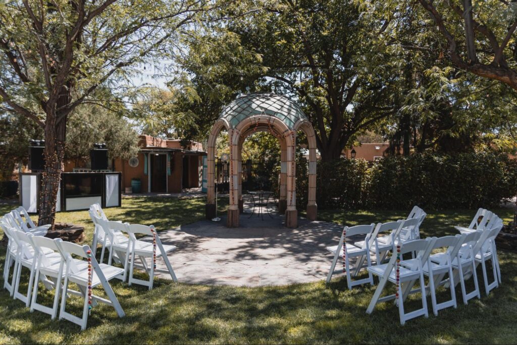 Small outdoor ceremony site with white chairs arranged around a unique gazebo surrounded by trees and greenery.