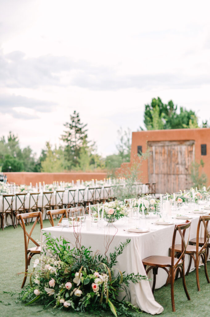 An elegant outdoor reception setup at Bishop's Lodge Santa Fe, NM, featuring long tables, candles, and floral arrangements.