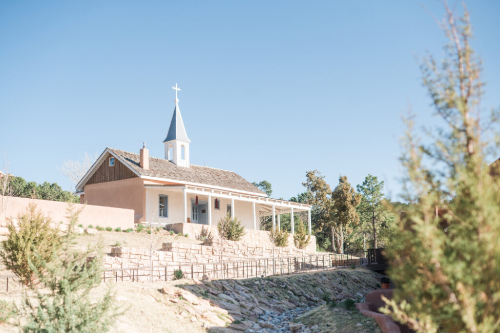 A historic chapel with a steeple at Bishop's Lodge Santa Fe, NM, set against a clear blue sky.