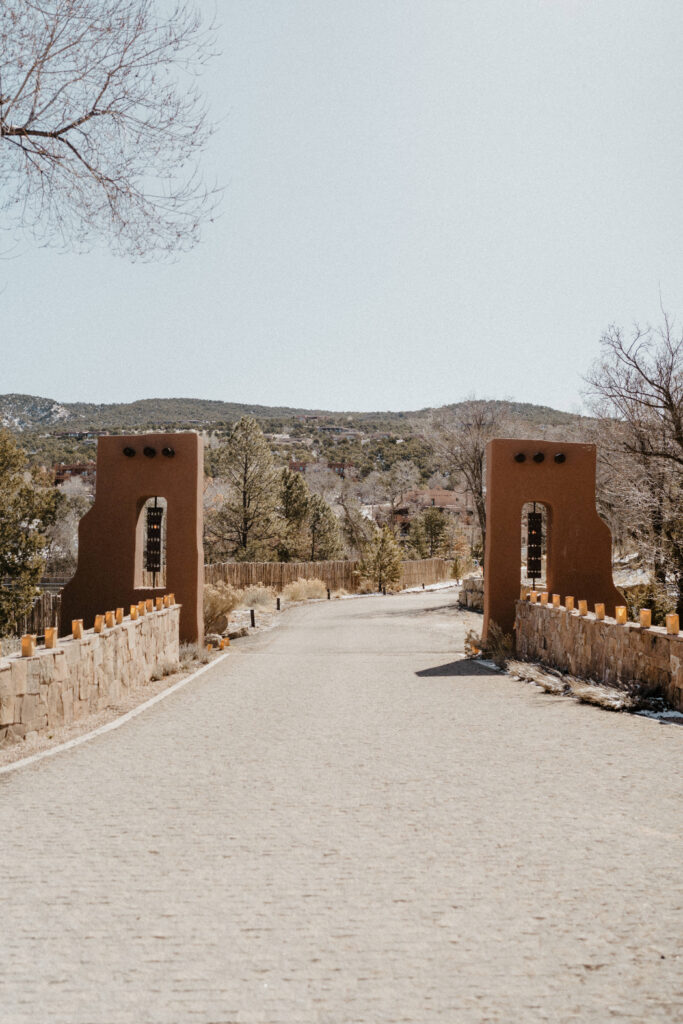 A scenic entrance to Bishop's Lodge Santa Fe, NM, with adobe archways, lanterns, and a winding road.