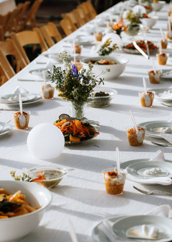 A long wedding table set with salads, small appetizers, and floral centerpieces in natural light.