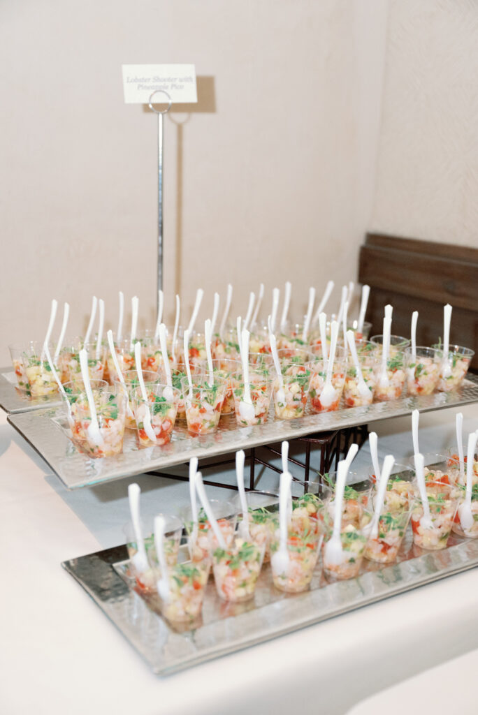 A catering display with mini lobster shooters in clear cups, each with a white spoon.