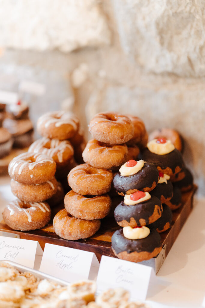 A dessert table featuring cinnamon sugar donuts, chocolate donuts, and labeled mini pastries.