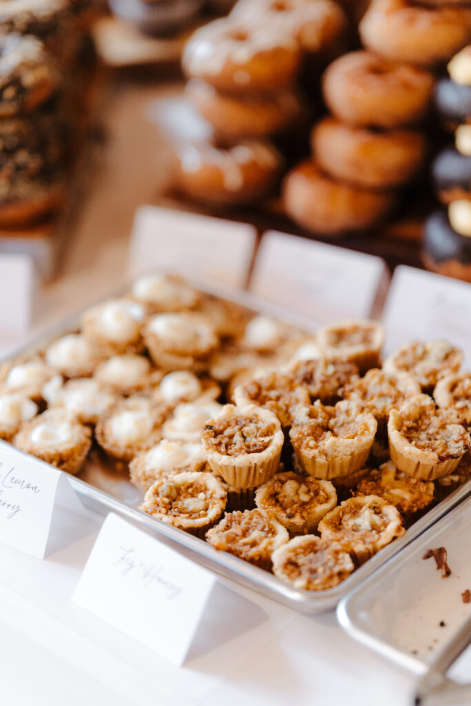 A tray of assorted mini pies and tarts with labels on a dessert table.