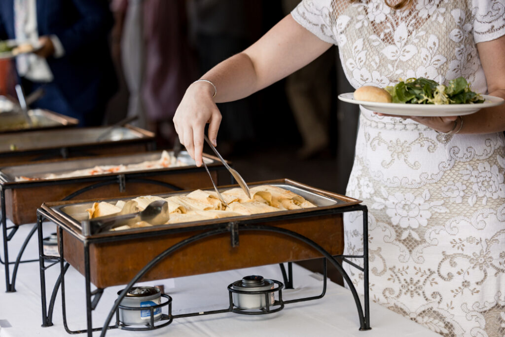 A wedding buffet with a guest serving themselves tamales, salad, and a bread roll.