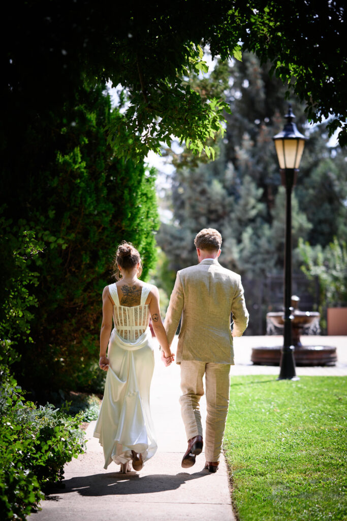 A bride and groom walk hand in hand down a garden pathway.