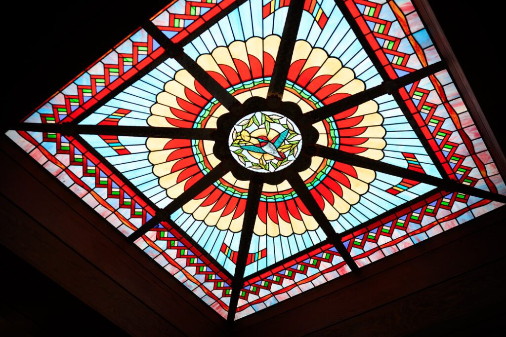 A stained-glass ceiling panel at La Fonda on the Plaza with a geometric pattern in red, blue, and gold features a hummingbird at its center.