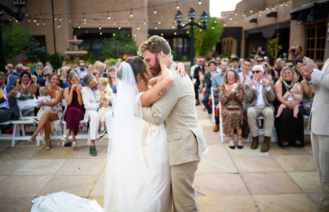 A bride and groom share their first kiss as a married couple in an outdoor courtyard ceremony.