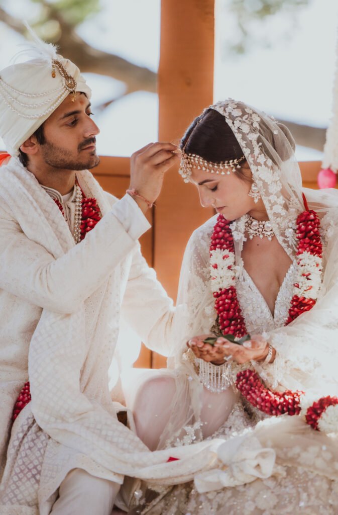 Groom applies sindoor on bride’s forehead during a traditional Indian wedding ceremony.