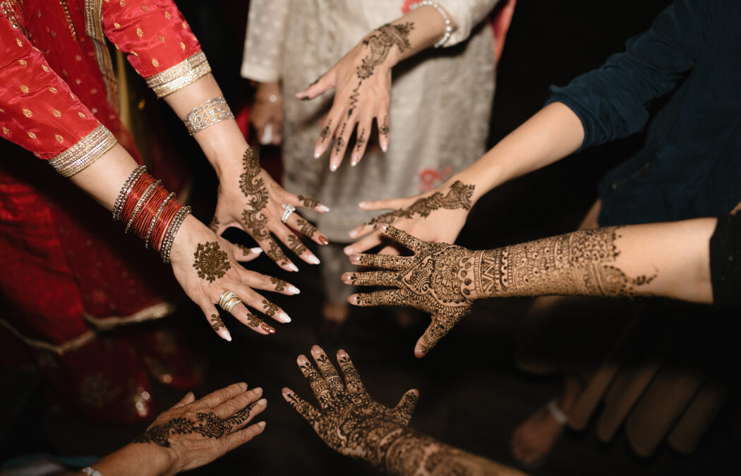 Hands adorned with intricate henna designs are displayed in a circle.