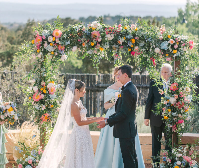 Bride and groom exchange vows in Santa Fe, surrounded by a floral arch made by one of the best Albuquerque florists.