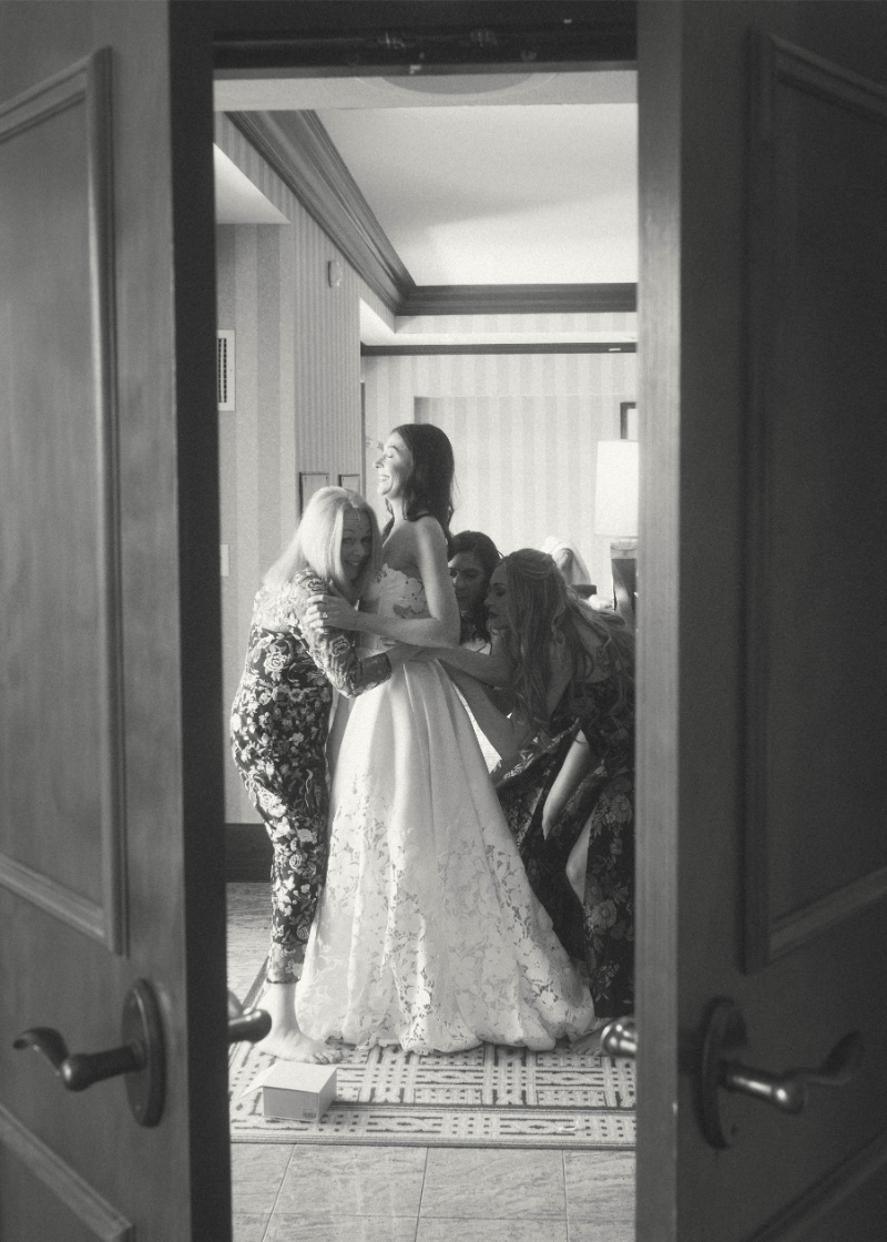 Bridesmaids help bride get into wedding dress.