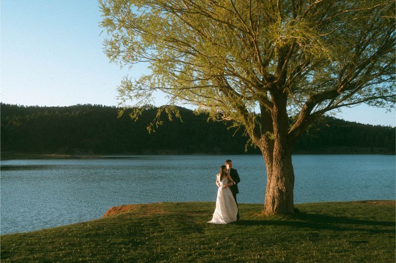 Bride and groom take golden hour wedding portraits in front of lake.