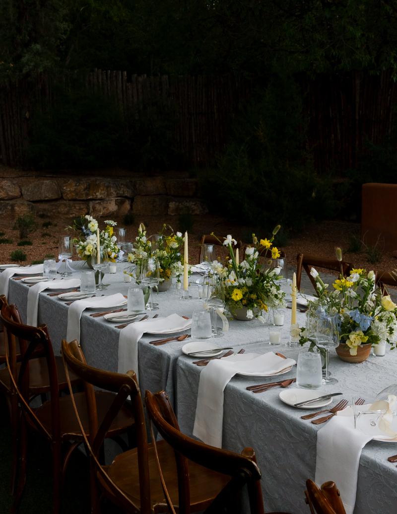 Table setting for reception at Bishop's Lodge in Santa Fe with light blue tablecloth, place setting for guests, and low floral arrangements.