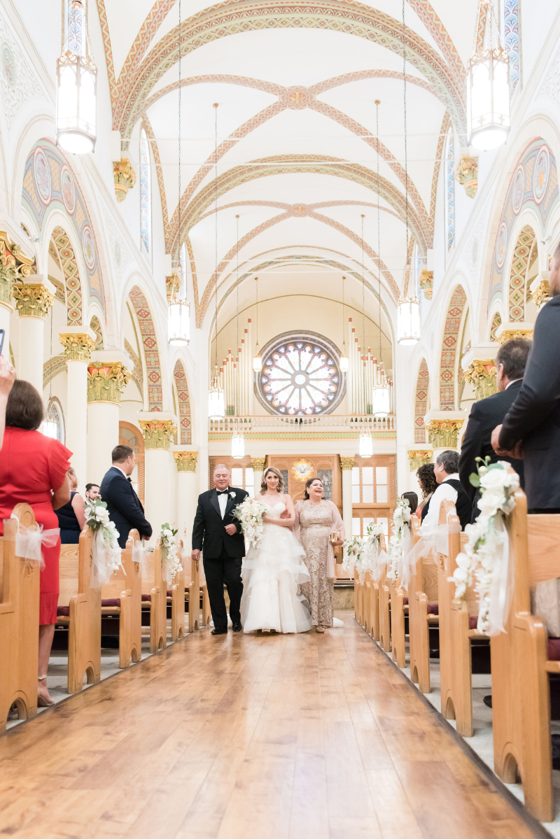 Bride walks down the aisle of Loretto Chapel with her father.