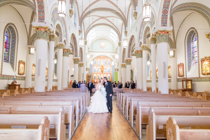 Bride and groom pause for kiss in the middle of the aisle after their Loretto Chapel wedding.