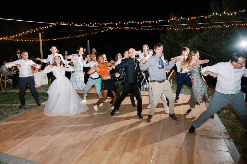 Wedding reception guests dance on wooden dance floor.